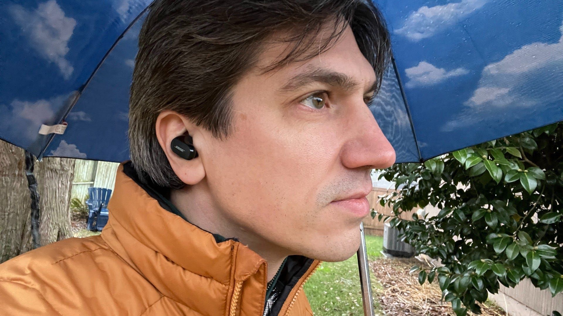 Close up of man listening to Bose QuietComfort Earbuds 2 in yard wearing gold jacket