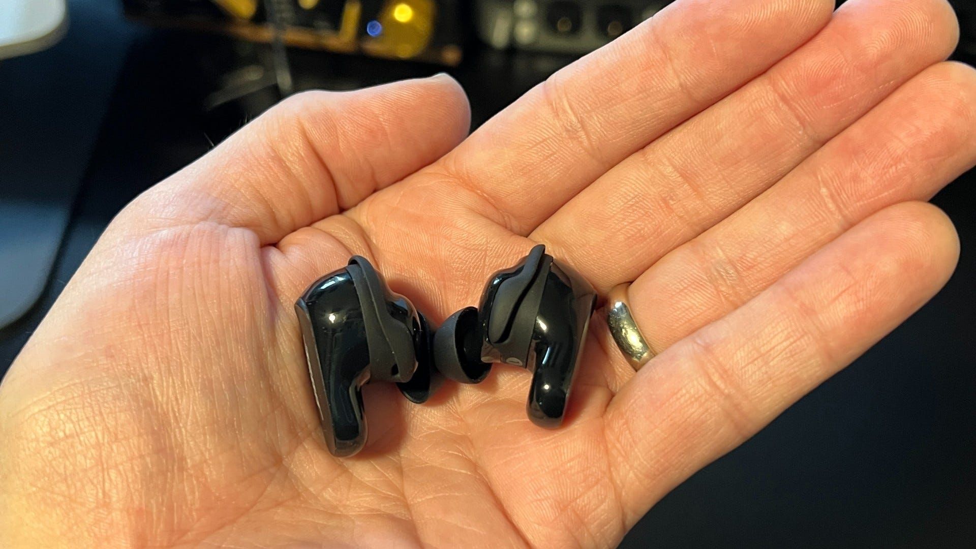 Bose QuietComfort 2 earbuds in hand above black desk