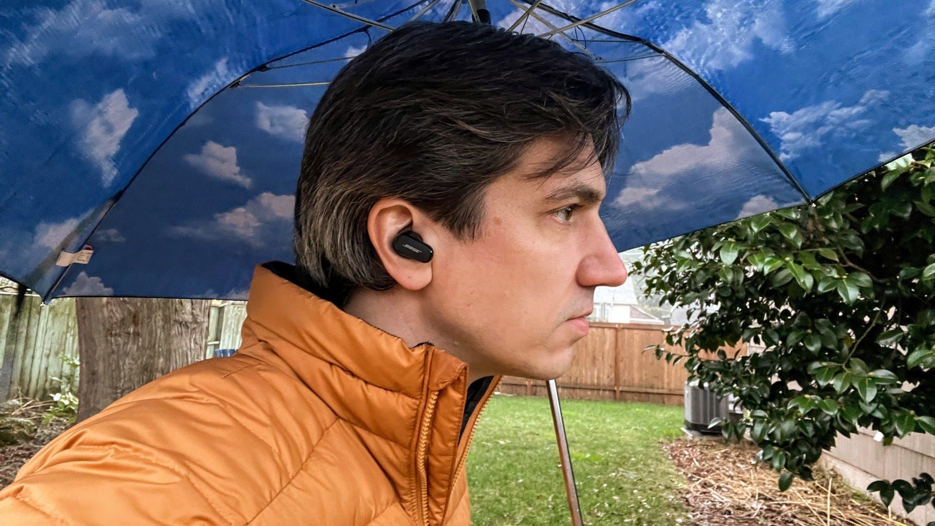 Man Listening to Bose QuietComfort 2 earbuds in yard with gold jacket