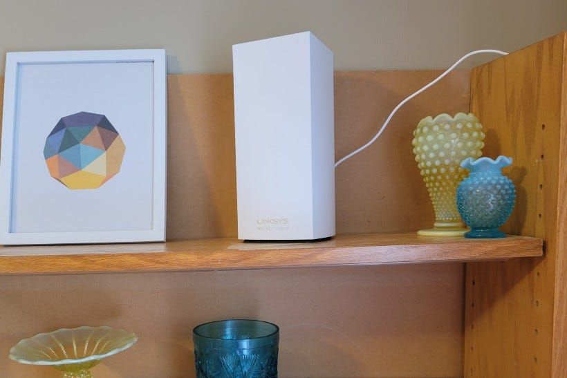 The LinkSYS Atlas 6E router on a shelf between a vase and a picture